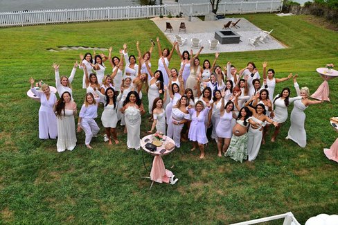 Women in white raising their arms together on the lawn