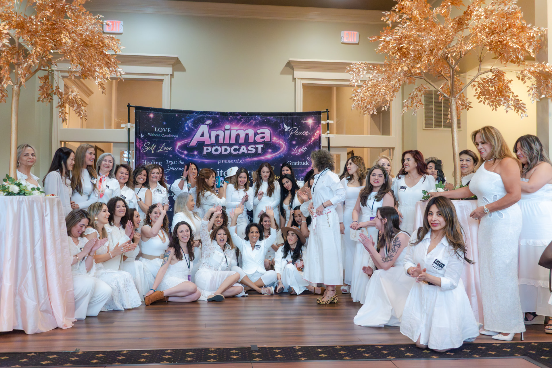 Women in white celebrating in front of the ÁNIMA Podcast banner at The White Party for the Soul